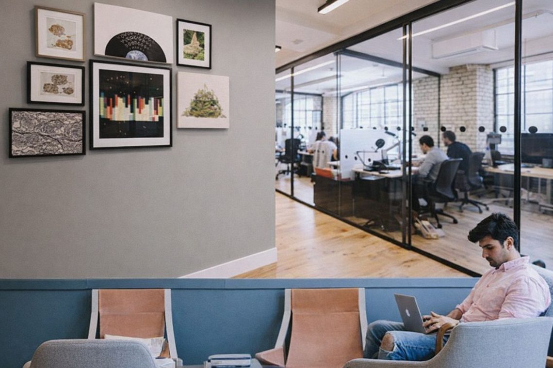 Man arbetar vid laptop i ett ljust coworking-utrymme med glastäckta kontor.