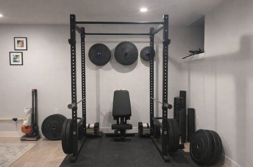 Svart skivstångsställning med träningsbänk och viktskivor i ett hemmagym.